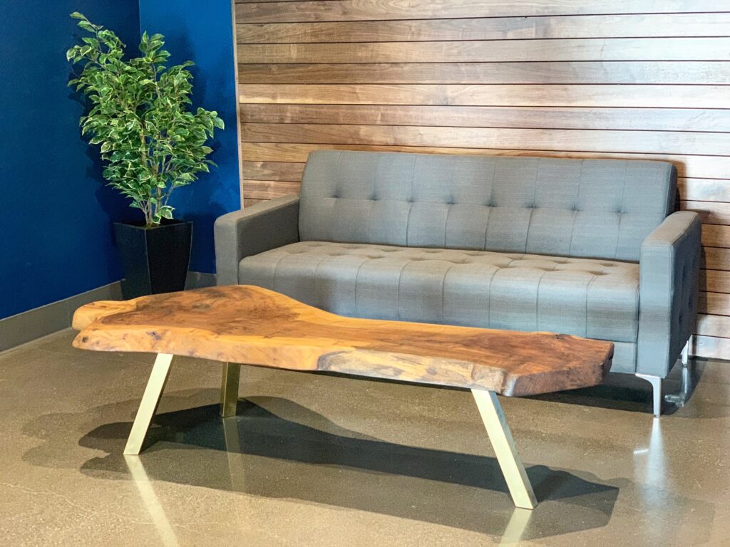 Live edge coffee table in Ottawa with golden legs, placed in front of a grey sofa and wooden accent wall.
