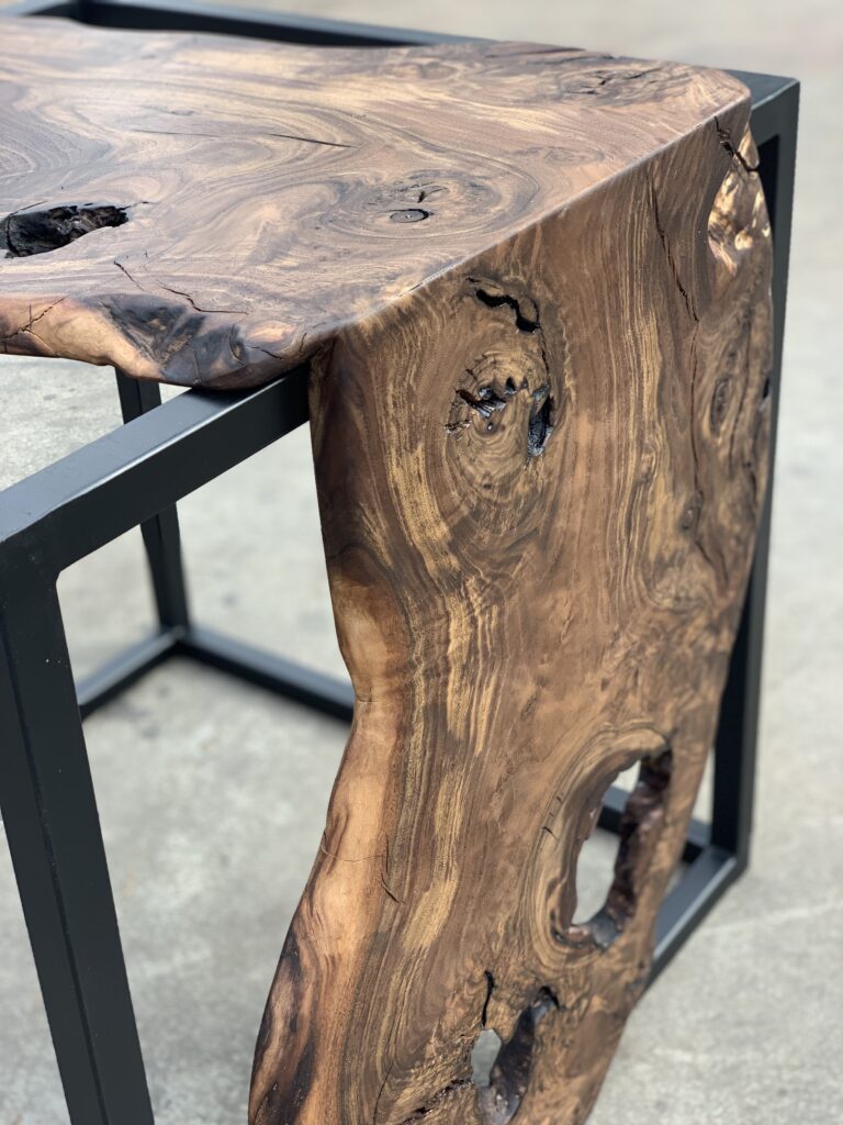 Close-up of a handcrafted live edge table with a natural wood slab and metal base.