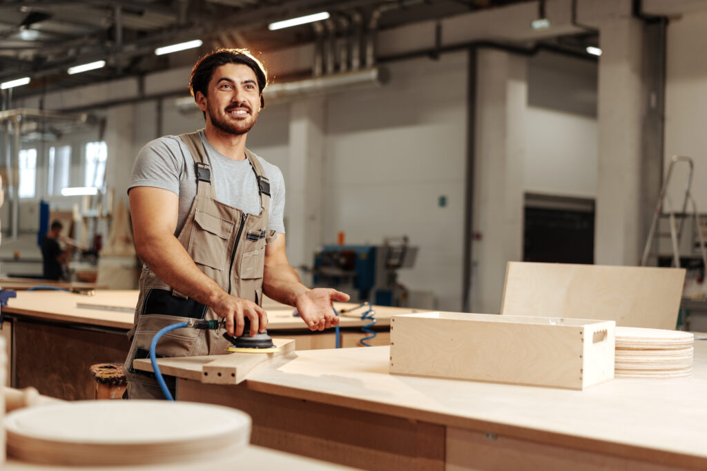 Smiling woodworker sanding wood in a modern Ottawa workshop where live edge tables are crafted